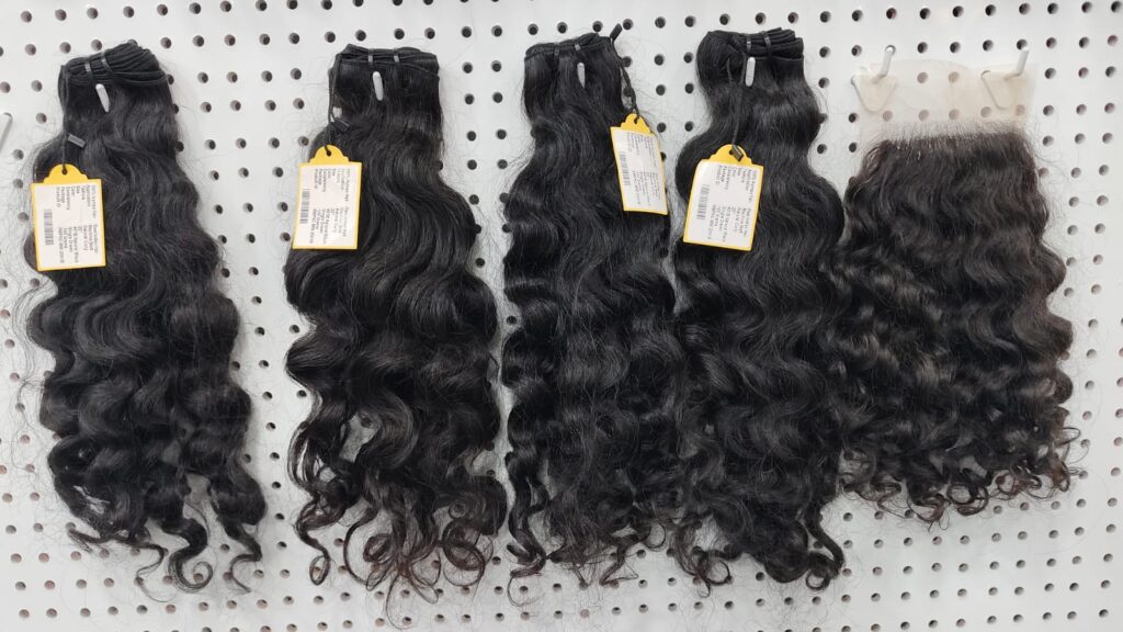 Virgin Remy human hair: four single-donor curly bundles and a lace closure on a display wall at Tirumala Hair